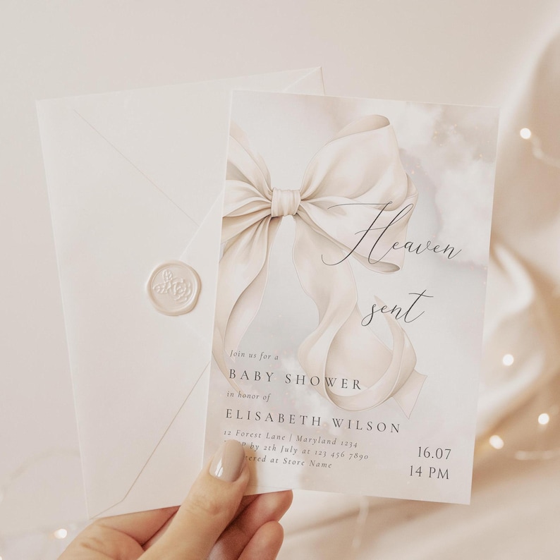 May include: A white baby shower invitation with a watercolor background and a large white bow. The text "Heaven sent" is written in cursive on the invitation. The invitation includes the details of the baby shower, including the date, time, and location.