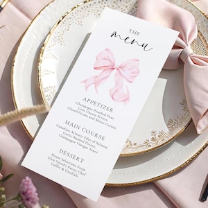 Op de afbeelding: Een witte menukaart met een roze aquarel strik illustratie. Het menu bevat opties voor voorgerechten, hoofdgerechten en desserts. De kaart ligt op een wit bord met een gouden rand, naast een roze servet.