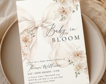 Puede incluir: Una invitación a una fiesta de bienvenida al bebé con una ilustración de acuarela de un lazo blanco con flores rosa pálido y el texto "Baby in Bloom". La invitación incluye la fecha, la hora, el lugar, la información de RSVP y el nombre de la persona que se celebra: Theresa Williams.