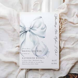 May include: A white bridal shower invitation with a blue watercolor bow and the text "Something Blue Before I Do!"  Join us for a Bridal Shower in honor of Katherine Wilson. 12 Forest Lane, Maryland 1234. RSVP by 12th July at 123 456 7890. Registered at Store Name. 16.07 14 PM.