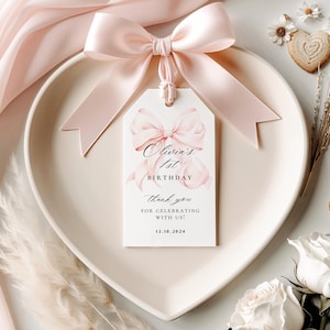 Pode incluir: Uma etiqueta de agradecimento rosa e branca com um la&ccedil;o rosa e o texto "Olivia's 1st Birthday Thank you for celebrating with us! 12.10.2024"