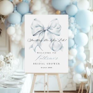 May include: A white sign with a blue watercolor bow and the text "Something blue before I do!"  Welcome to Kathrine's Bridal Shower 16 July 20XX.