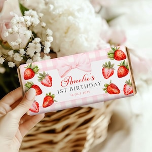May include: Pink and white gingham chocolate bar wrapper with a pink bow and strawberries. The wrapper says "Amelie's 1st Birthday 16 Oct 2025".