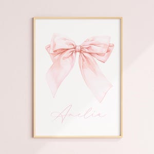 May include: A pink watercolor bow with the name Amelia written in pink script below it.