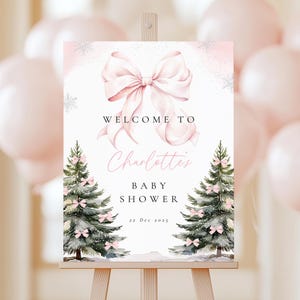 May include: A baby shower welcome sign on an easel. The sign features a large pink bow, the words "Welcome to Charlotte's Baby Shower", and two decorated Christmas trees. The date "22 Dec 2025" is also displayed.