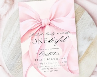 以下が含まれることがあります： ピンクの水彩画のリボンに「Isn't she lovely, isn't she ONEderful」と「Join us to celebrate Charlotte's FIRST BIRTHDAY」のテキストとイベントの詳細が書かれています。