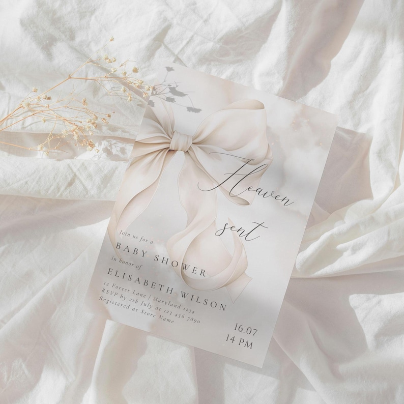 May include: A white baby shower invitation with a watercolor illustration of a large white bow and the text "Heaven sent". The invitation includes the text "Join us for a Baby Shower in honor of Elisabeth Wilson" and the date and time of the event.