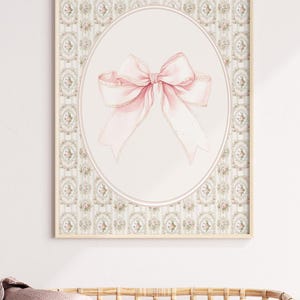 May include: A framed print with a pink bow on a white background. The frame has a light wood finish and the background is a light green and white floral pattern.