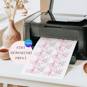 May include: A black printer printing sheets of pink bow-themed labels. Each label features a watercolor bow design and text. The image also shows a vase with dried flowers and a decorative basket.