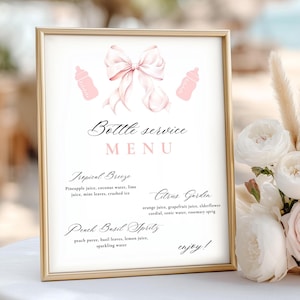 May include: A framed menu with a gold border, featuring a pink bow and baby bottle illustrations. The menu lists drink options like Tropical Breeze and Citrus Garden. The text "Bottle service MENU" is at the top.