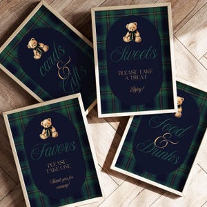 May include: Four framed signs with a navy blue oval design, a teddy bear illustration, and text in elegant script. The signs are set against a green and navy plaid background. The text includes "Cards & Gifts", "Sweets", "Favors", and "Food & Drinks".