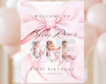May include: A pink and white welcome sign for a first birthday celebration. The sign features a large pink bow, the words "Welcome to" and "First Birthday", the name "Briar Rose's", the word "One" with photos, and the date August 12, 2025.