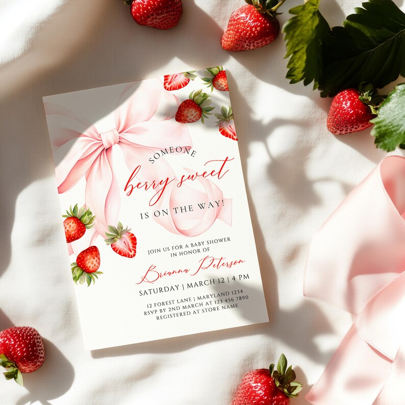 May include: A baby shower invitation with a watercolour design. The invitation features a pink bow, strawberries, and the text "Someone berry sweet is on the way!" Fresh strawberries surround the invitation.
