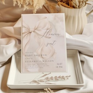 May include: A baby shower invitation with a watercolor background featuring a white bow and the text "Heaven sent". The invitation includes the date, time, and location of the event, as well as the name of the guest of honor, Elisabeth Wilson.