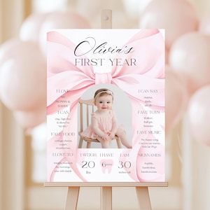 Könnte beinhalten: Ein rosa-weißes Schild zum ersten Geburtstag auf einer Staffelei. Das Schild zeigt ein Babyfoto, den Text "Olivia's FIRST YEAR" und Details wie Gewicht (9,07 kg), Größe (76,2 cm) und Lieblingsdinge.