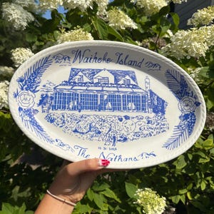 May include: Oval white ceramic platter with a blue illustration of a building and the text "Waiheke Island". The platter also features floral and foliage designs, and the text "The Nathans 12-31-2015".