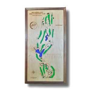 Puede incluir: Un mapa enmarcado de madera del Oklahoma City Golf & Country Club en Nichols Hills, Oklahoma. El mapa muestra el diseño del campo de golf con calles verdes, obstáculos de agua azules y búnkeres de arena blanca. El mapa está firmado por Jeff McDougall.