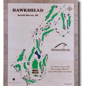 May include: A wooden map of the Hawkshead Golf Course in South Haven, Michigan. The map shows the layout of the course with green and brown colors. The text "The Home Course Of "The Longest Driver" Alexandria Bain Van Slyke" is printed on the map.