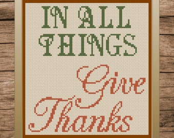 May include: A framed cross-stitch with the text "In all things give thanks" in green and orange lettering on a beige background.