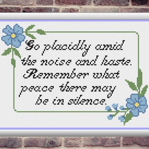 May include: Cross-stitch framed artwork with the text "Go placidly amid the noise and haste. Remember what peace there may be in silence." The design includes blue floral accents and a light blue border.