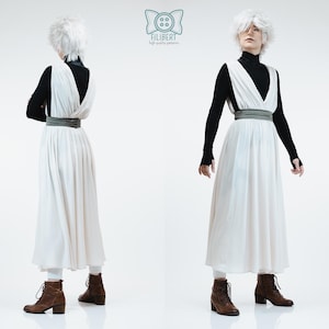 May include: A white sleeveless dress with a deep V-neckline and a wide grey waistband, worn over a black long-sleeved turtleneck shirt. The outfit includes white leggings and brown lace-up boots. The Filibert logo is visible at the top center.
