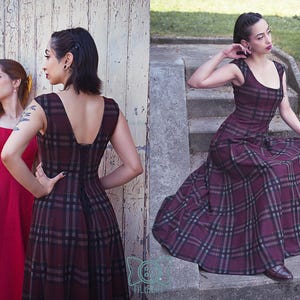 May include: Two women in dresses. One in a red dress, the other in a burgundy plaid dress with a scoop neckline and a flared skirt. The plaid dress has a black and gray pattern. The woman in the plaid dress is sitting on concrete steps.