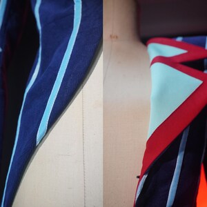 Pode incluir: Close-up de um casaco azul marinho com detalhes em azul claro e vermelho. O casaco apresenta riscas azuis claras e um design geom&eacute;trico na gola. O tecido parece ser um material texturizado.