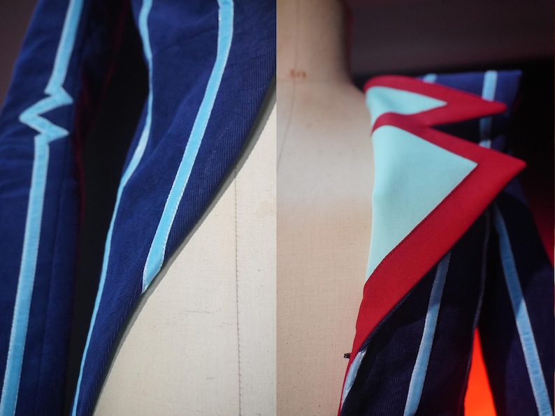 Pode incluir: Close-up de um casaco azul marinho com detalhes em azul claro e vermelho. O casaco apresenta riscas azuis claras e um design geom&eacute;trico na gola. O tecido parece ser um material texturizado.