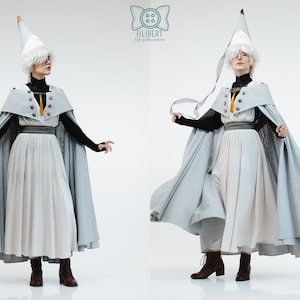 May include: A costume set featuring a light blue cape with gold buttons and a yellow tassel, a white pleated skirt, a black long-sleeved top, and a pointed white hat. The Filibert logo is visible at the top center of the image.