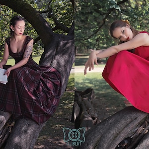 May include: Two women wearing dresses are sitting on a tree branch in a park. One woman is wearing a burgundy plaid dress, and the other is wearing a red dress. The dresses are the focal point of the image, showcasing their design and color.