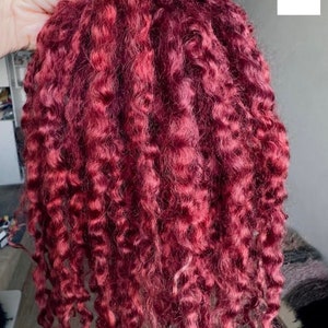 Peut inclure: Un paquet d'extensions de cheveux rouge bordeaux profond pr&eacute;sentant une texture serr&eacute;e, enroul&eacute;e et boucl&eacute;e. Les m&egrave;ches de cheveux sont de couleur uniforme et dispos&eacute;es en longues boucles en cascade tombant verticalement.