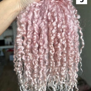 Peut inclure: Un faisceau de fibres boucl&eacute;es rose clair, douces et dot&eacute;es d'un &eacute;clat lustr&eacute;. La texture est tr&egrave;s enroul&eacute;e, en forme de petites boucles, passant d'un rose pastel uni sur le dessus &agrave; une teinte plus claire, presque blanche, aux extr&eacute;mit&eacute;s.
