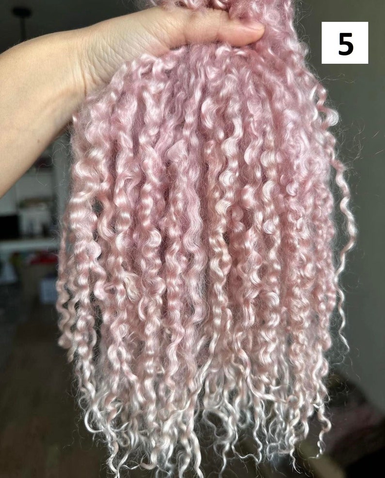 Peut inclure: Un faisceau de fibres boucl&eacute;es rose clair, douces et dot&eacute;es d'un &eacute;clat lustr&eacute;. La texture est tr&egrave;s enroul&eacute;e, en forme de petites boucles, passant d'un rose pastel uni sur le dessus &agrave; une teinte plus claire, presque blanche, aux extr&eacute;mit&eacute;s.
