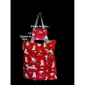 May include: A red and white reusable shopping tote bag with a pattern of dogs. The bag folds into a small, compact pouch with a zipper closure. The text "Opens to this..." and "Folds to this..." is printed on the image.