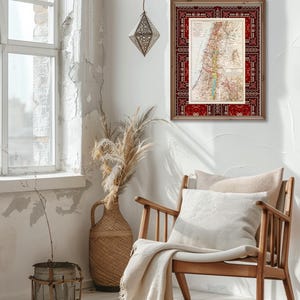 May include: A vintage map of Palestine framed in a red and brown wood frame with a patterned border. The map is printed on paper with a cream background and features a detailed outline of the region with various geographical features labeled in black text. The frame is hanging on a white wall in a room with a wooden chair and a wicker vase with dried flowers.