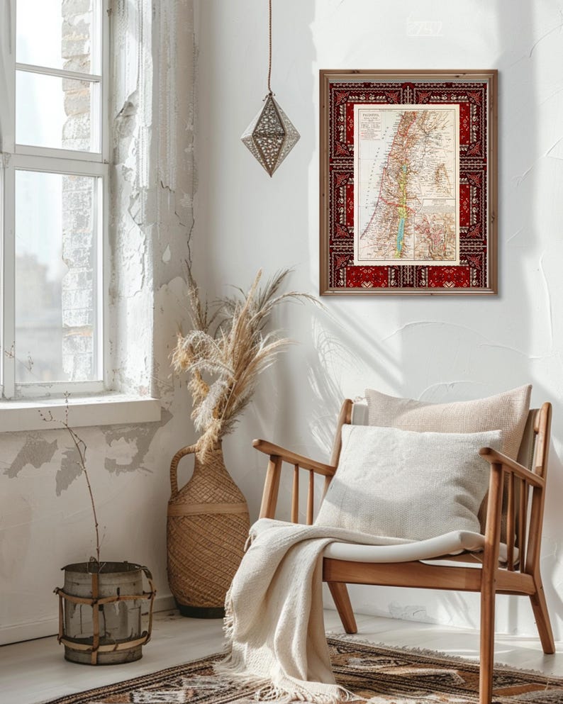 May include: A vintage map of Palestine framed in a red and brown wood frame with a patterned border. The map is printed on paper with a cream background and features a detailed outline of the region with various geographical features labeled in black text. The frame is hanging on a white wall in a room with a wooden chair and a wicker vase with dried flowers.