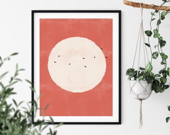 May include: A minimalist art print featuring a large white circle on a coral background with a flock of black birds flying across the circle.