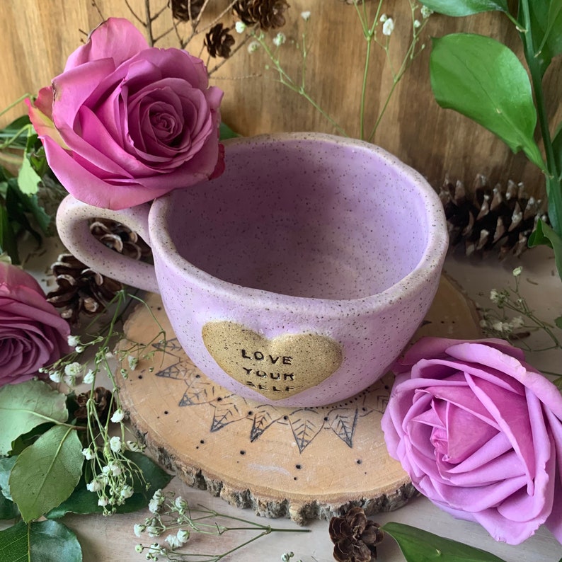 May include: Purple ceramic mug with a gold heart that says "Love Your Self" on a wooden coaster with a mandala design.