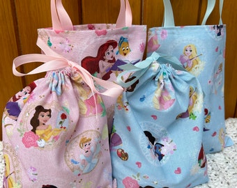 May include: Three different fabric bags with Disney Princesses on them. Two are drawstring bags and one is a tote bag with handles. The drawstring bags are pink and blue with a white background. The tote bag is pink with a white background.