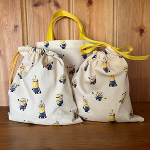May include: Two yellow and white drawstring bags with a Minion pattern. The larger bag has yellow handles.