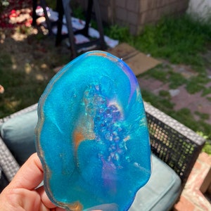 Könnte beinhalten: Ein blauer, violetter und goldener Agat-Untersetzer mit einem einzigartigen, natürlichen Muster. Der Untersetzer ist aus Harz gefertigt und hat eine glänzende Oberfläche.