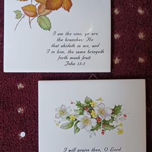 Puede incluir: Dos baldosas de cerámica blancas con diseños florales y texto religioso. Una baldosa presenta una rama con hojas marrones y verdes y el texto "Yo soy la vid, vosotros los pámpanos..." de Juan 15:5. La otra baldosa tiene flores blancas y el texto "Te alabaré, oh Señor..." del Salmo 86:12.
