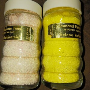 Puede incluir: Dos frascos de vidrio vintage de productos de baño Helena Rubinstein. Uno contiene gránulos rosas y está etiquetado como "Blossom Time Foam Bath". El otro contiene gránulos amarillos y está etiquetado como "Command Perfumed Foam".