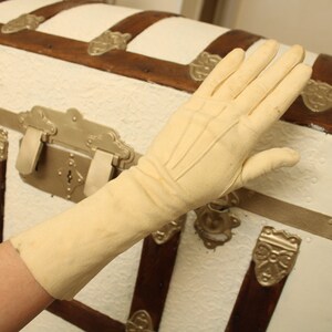 May include: A pair of long, cream-colored gloves made of a soft, smooth fabric. The gloves have a subtle sheen and are slightly wrinkled.
