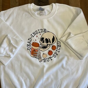 May include: White sweatshirt with a graphic of a skull holding a coffee cup with the text "Dead inside but-spiced".