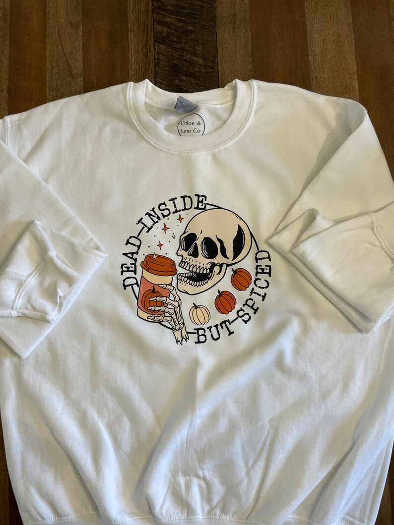 May include: White sweatshirt with a graphic of a skull holding a coffee cup with the text "Dead inside but-spiced".