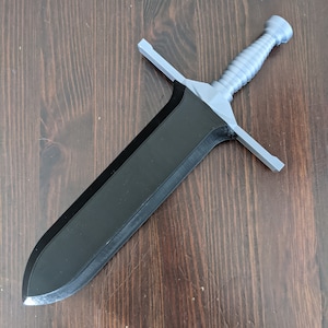 May include: A black and silver sword with a textured handle. The sword has a pointed tip and a straight blade.