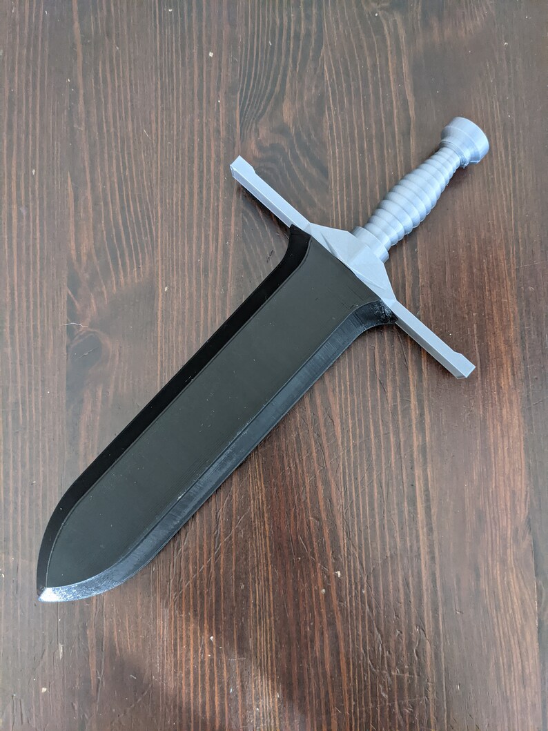 May include: A black and silver sword with a textured handle. The sword has a pointed tip and a straight blade.