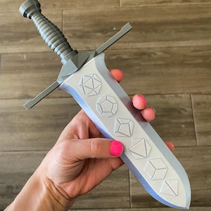May include: A silver-colored sword with a decorative handle and a blade featuring a series of embossed geometric shapes.