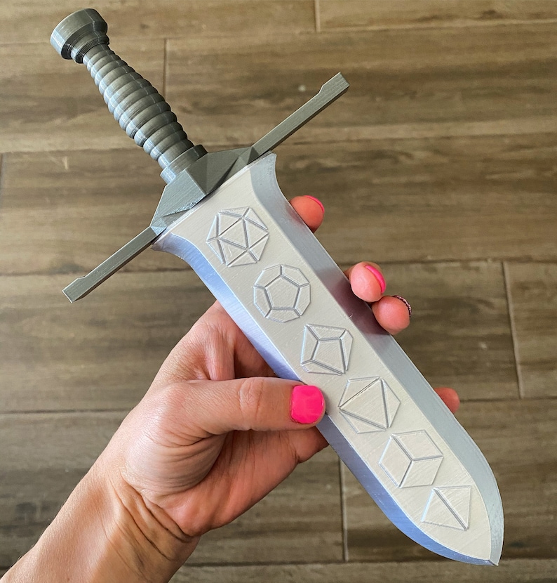 May include: A silver-colored sword with a decorative handle and a blade featuring a series of embossed geometric shapes.